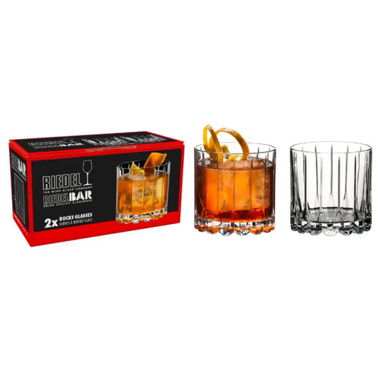 A RIEDEL Rocks Glass Barware Drink Specific Glassware Set of 2 by Riedel is pictured, featuring two elegant crystal rocks glasses—one empty, the other filled with an orange cocktail garnished with citrus—making it a perfect showcase for sophisticated cocktail glassware.
