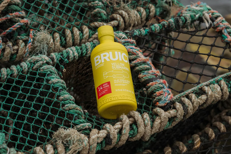 Load image into Gallery viewer, A bottle of Bruichladdich Yellow Submarine III 14 Year Old Islay Single Malt Scotch Whisky rests outdoors on stacked fishing nets with rope and mesh.
