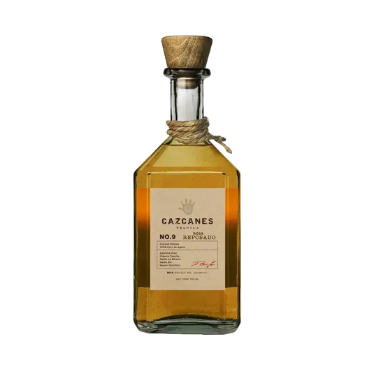 A glass bottle of Cazcanes Rosa Reposado No. 9 Tequila with a wooden stopper and a tan label detailing production information and a hand-print logo.