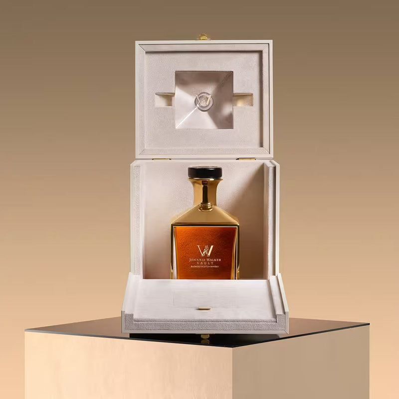 Load image into Gallery viewer, A luxurious bottle of Johnnie Walker Vault: The Couture Blend Olivier Rousteing 700ml is displayed in an elegant cream-colored box with a satin interior, set atop a reflective black and gold pedestal against a gradient beige background.
