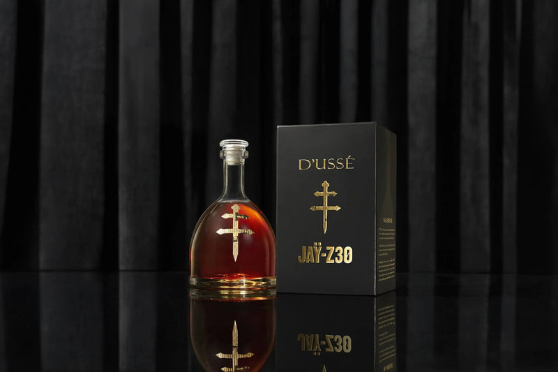 Load image into Gallery viewer, A bottle of D’USSÉ VSOP Jay-Z30 Limited Edition Cognac (PRE-ORDER) stands beside its striking black and gold box, set against a vertically striped black background, showcasing this exclusive collaboration from D’USSÉ.
