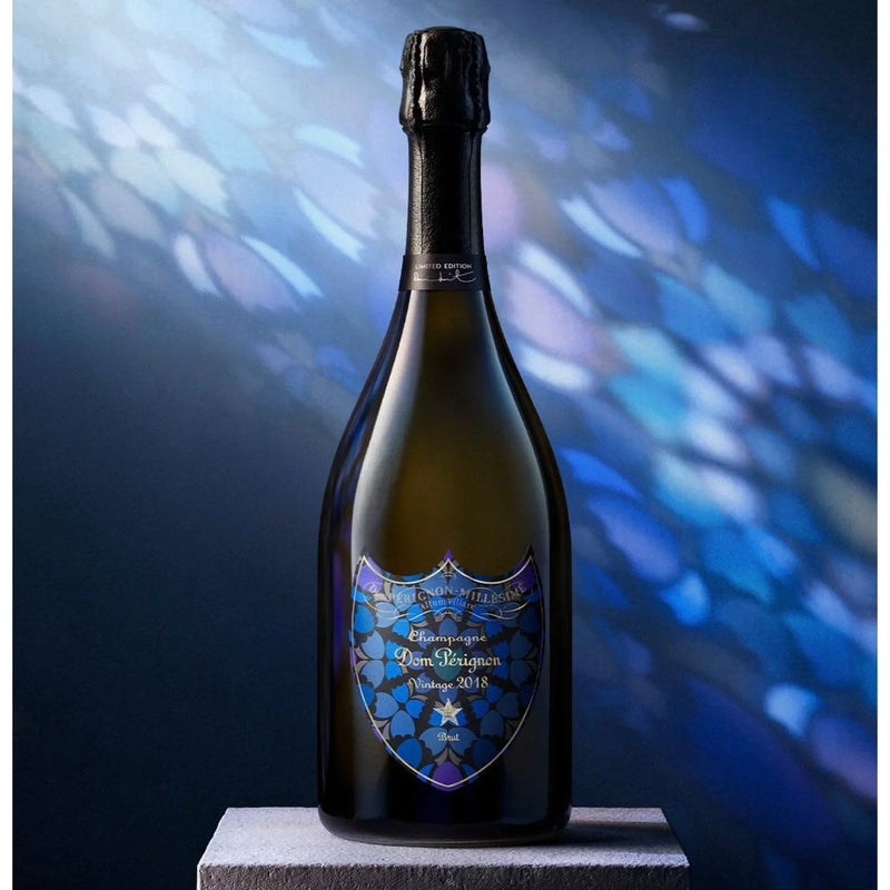 Load image into Gallery viewer, Dom Pérignon Vintage 2018 Damien Hirst Limited Edition Brut Champagne bottle with a dark glass body and a label featuring a blue and black floral motif, standing on a stone pedestal.
