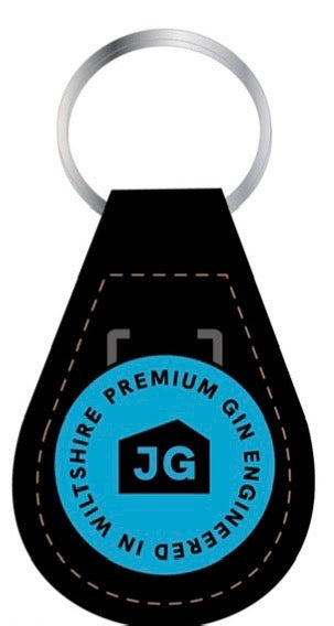 Load image into Gallery viewer, The James Gin The Tupac 2 Bottle Set W/ Souvenir Gift Key Chain by James Gin US includes a black leather keychain with brown stitching and a blue emblem reading 'PREMIUM JAMES GIN ENGINEERED IN WILTSHIRE' with 'JG' in a house icon, reflecting British craft gin quality.
