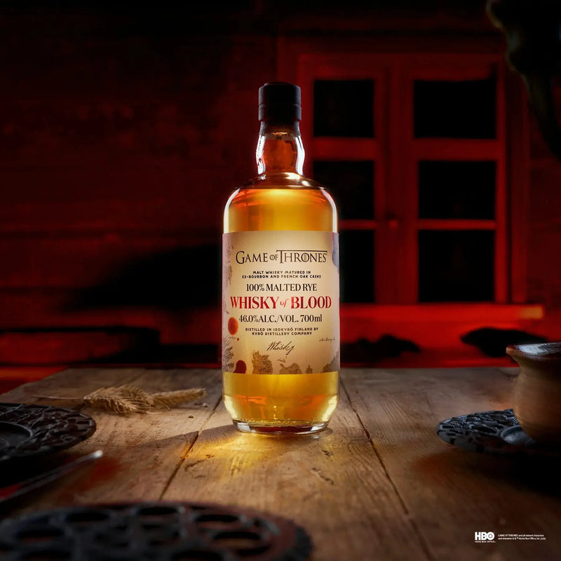 Load image into Gallery viewer, A Kyrö x Game of Thrones Whisky of Fire &amp; Blood Bundle (PRE-ORDER) from Main Street Liquor rests on a wooden table in a dimly lit room, red light streaming through the window and plates and cloth enhancing the mysterious ambiance.
