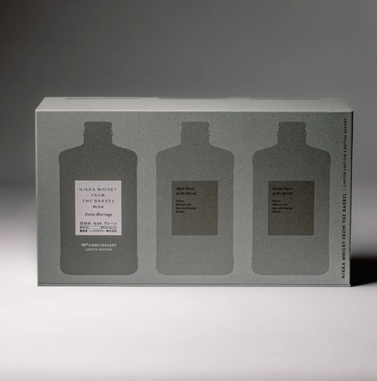 A rectangular gray box labeled "Nikka From The Barrel Extra Marriage Gift Set" by Nikka features silhouettes of three bottles, with extra detail on the center one. Soft lighting casts gentle shadows behind this Japanese whisky collector’s set.