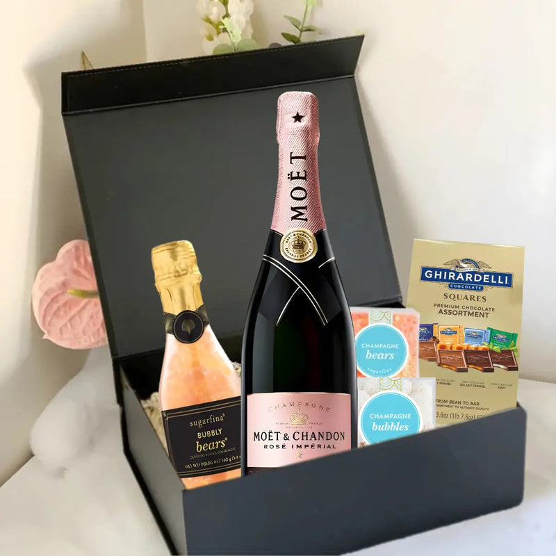 Load image into Gallery viewer, The Premium Champagne Gift Box by Main Street Liquor features a bottle of Moët &amp; Chandon Rosé, a mini sparkling wine, Ghirardelli chocolate squares, and champagne-flavored gummies in a luxurious black box on a white surface.
