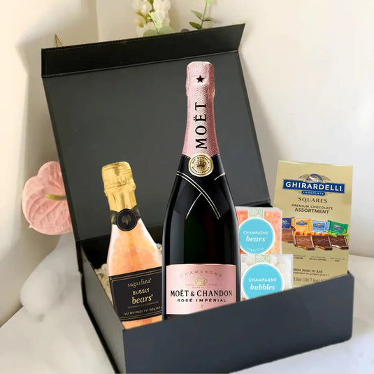 The Premium Champagne Gift Box by Main Street Liquor features a bottle of Moët & Chandon Rosé, a mini sparkling wine, Ghirardelli chocolate squares, and champagne-flavored gummies in a luxurious black box on a white surface.