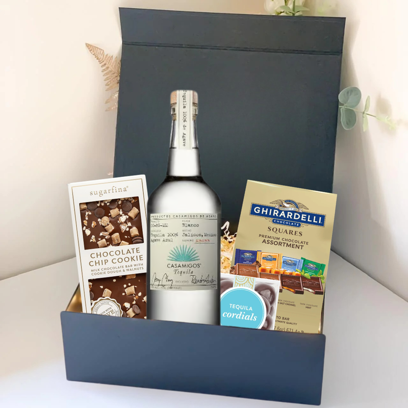 Load image into Gallery viewer, The Premium Tequila Gift Box by Main Street Liquor features Casamigos tequila, a Sugarfina chocolate chip cookie bar, and Ghirardelli gourmet chocolate squares, all upright in an elegant display.
