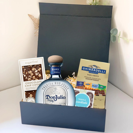The Premium Tequila Gift Box by Main Street Liquor includes Don Julio premium tequila, Ghirardelli gourmet chocolate, Sugarfina chocolate chip cookie candies, and tequila cordials, all elegantly arranged with decorative filler.