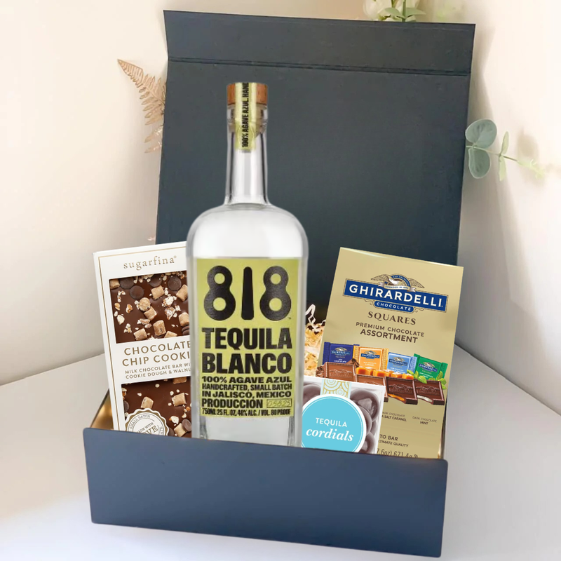 Load image into Gallery viewer, The Premium Tequila Gift Box by Main Street Liquor features 818 Tequila Blanco, Sugarfina chocolate chip cookies, and Ghirardelli squares, beautifully presented on a light surface with a leafy plant in the background.
