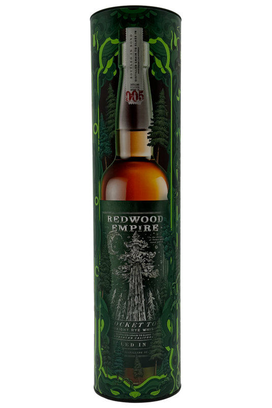 A cylindrical container holding Redwood Empire Whiskey’s Rocket Top Bottled in Bond Straight Rye Whiskey Batch 004 2025 Release, featuring a green forest-themed design and an illustrated redwood tree on the Sonoma County label.