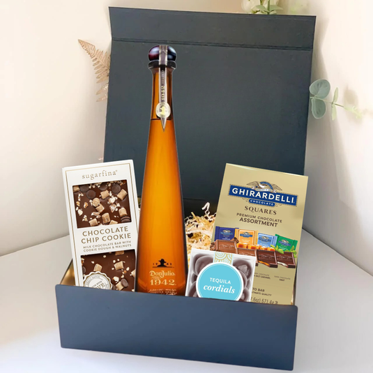 The Premium Tequila Gift Box by Main Street Liquor includes Don Julio 1942, Sugarfina chocolate chip cookie bites, Ghirardelli squares, and tequila cordials, all beautifully arranged on a white surface.