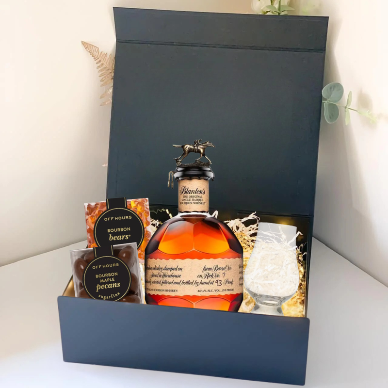 Load image into Gallery viewer, The Premium Bourbon Gift Box by Main Street Liquor includes a bottle of premium bourbon, a whiskey glass, and two packs of bourbon-flavored snacks, all elegantly packed in shredded material inside a sleek black box.
