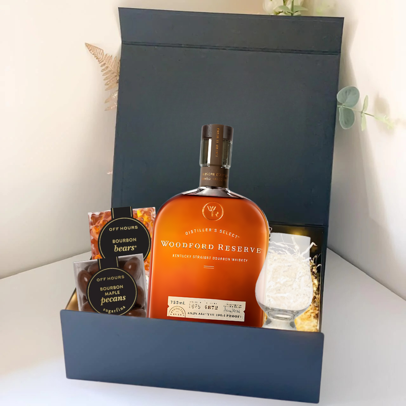 Load image into Gallery viewer, The Premium Bourbon Gift Box by Main Street Liquor features Woodford Reserve whiskey, a glass, bourbon bears gummies, and bourbon pecans—all elegantly arranged against a plain background.
