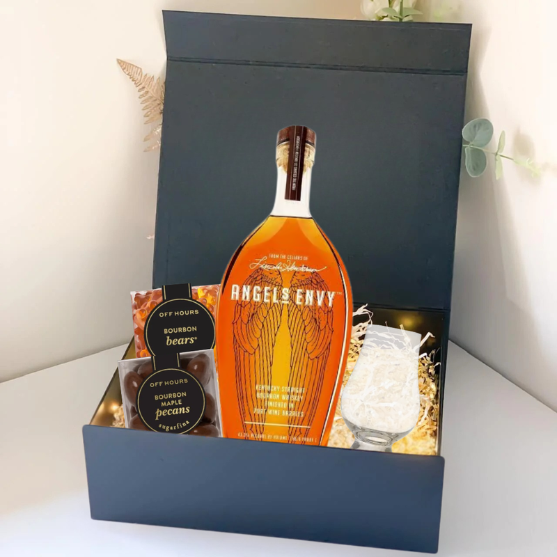 Load image into Gallery viewer, The Premium Bourbon Gift Box by Main Street Liquor includes an Angels Envy bottle, glass, filler, and two small containers labeled Off Hours Bourbon Bears and Pecans. The open box is displayed on a white surface.
