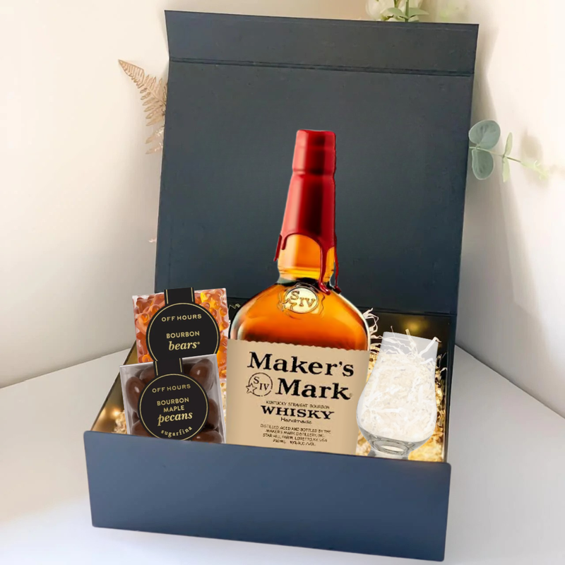 Load image into Gallery viewer, The Premium Bourbon Gift Box from Main Street Liquor features Maker’s Mark bourbon, a whiskey glass, pecans, bourbon bears, and a snack bar arranged with decorative lights in a sleek black gift box.
