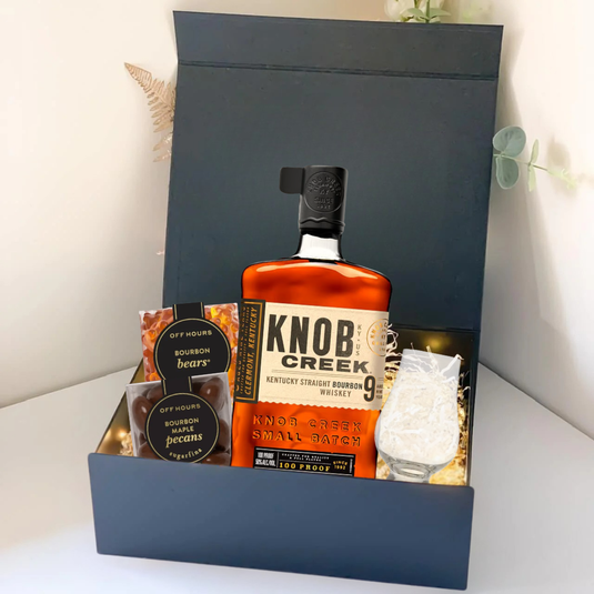 The Premium Bourbon Gift Box by Main Street Liquor features Knob Creek Kentucky Straight Bourbon, bourbon bears, bourbon pecans, and a glass with ice, all elegantly presented on a white surface.