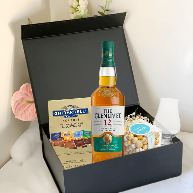 Load image into Gallery viewer, The Premium Scotch Gift Box by Main Street Liquor includes The Glenlivet 12-Year-Old Scotch, Ghirardelli chocolates, a glass, and mixed nuts, elegantly arranged with floral accents.
