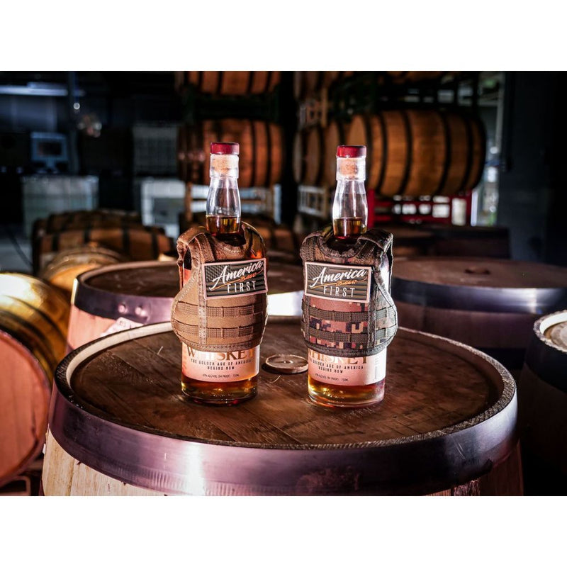 Load image into Gallery viewer, Six bottles of America First Straight Bourbon Whiskey from the America First brand are showcased on a wooden barrel, set within a distillery lined with aging Kentucky bourbon barrels in the background.
