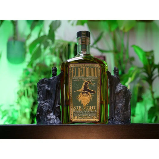 A bottle of Eldenwood Straight Bourbon Whiskey by Eldenwood, with Eryndor the Elder on the label, is placed between two dark bookends and framed by lush green plants in the background.