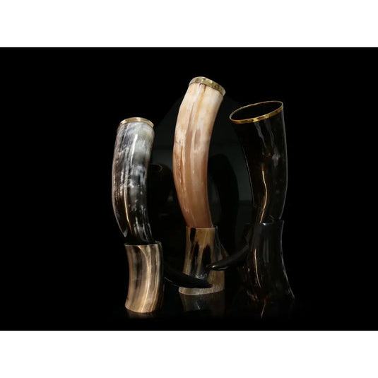 Three polished drinking horns—black, brown, and marbled white-gray—stand upright on black stands against a dark backdrop. Each shines with a metal rim, ready to be filled with Eldenwood Straight Bourbon Whiskey by Eldenwood.