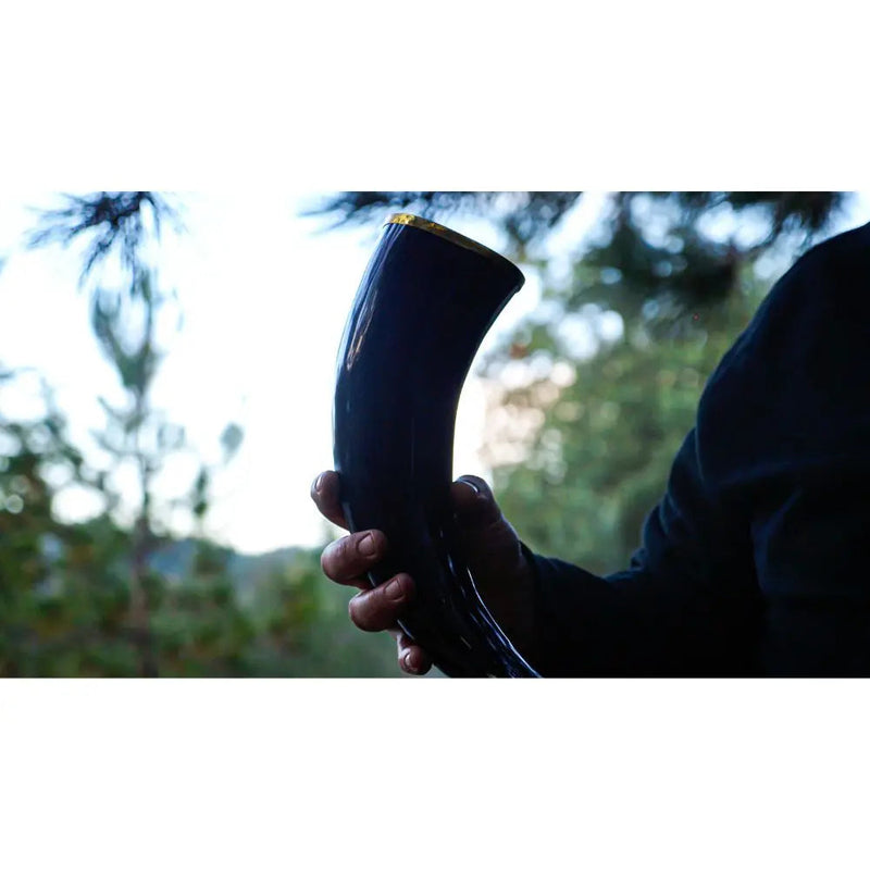 Load image into Gallery viewer, A person in a dark sleeve holds a polished drinking horn outdoors, savoring the moment as sunlight hits the greenery—perhaps toasting with Eldenwood Straight Bourbon Whiskey from Eldenwood among the blurred trees.
