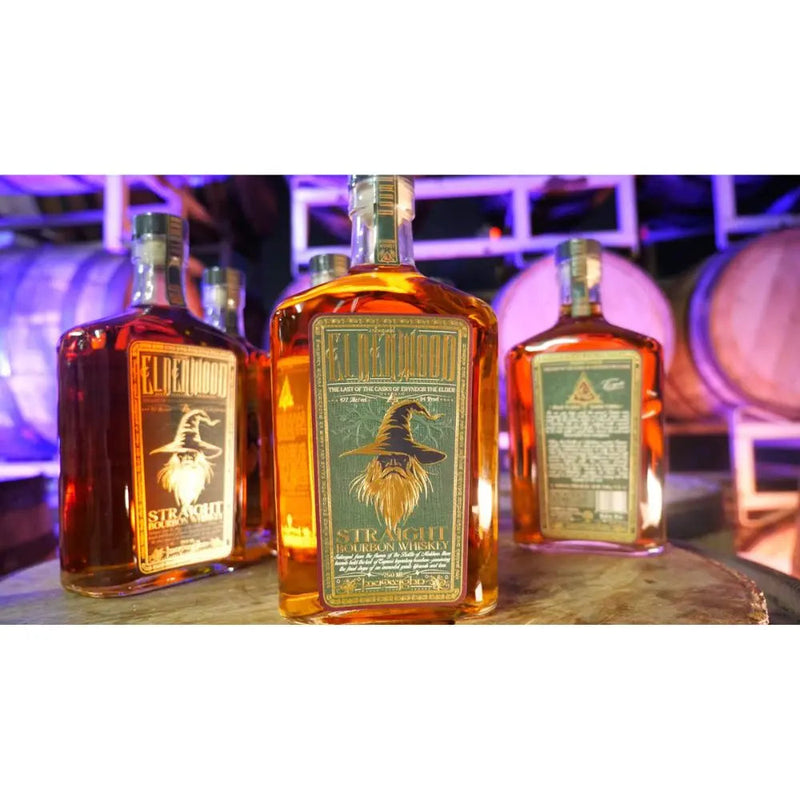 Load image into Gallery viewer, Three bottles of Eldenwood Straight Bourbon Whiskey are displayed on a barrel, with barrels and purple lighting behind them. The label shows Eryndor the Elder, a raven in a wizard hat, highlighting this enchanting whiskey from Eldenwood.
