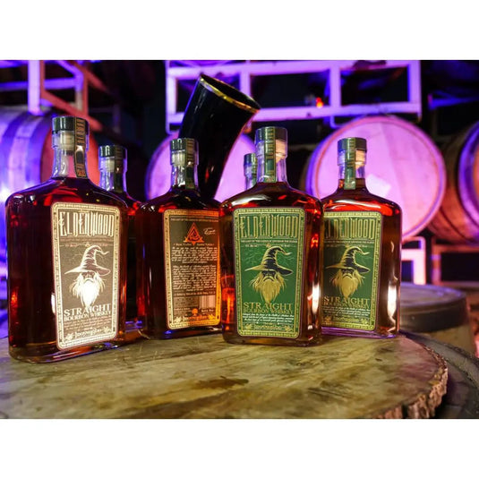 Four bottles of Eldenwood Straight Bourbon Whiskey, each featuring an illustrated raven label, are arranged on a wooden surface with aging barrels and purple lighting in the background.