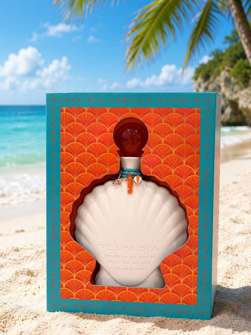Load image into Gallery viewer, A bottle of PLAYA DIA Blanco Tequila, crafted from 100% Blue Weber agave and entirely additive-free, rests in a shell-shaped box on a sandy beach with a palm tree and clear blue ocean in the background. The orange packaging with teal accents beautifully complements this exceptional spirit from Playa Dia Blanco Tequila.
