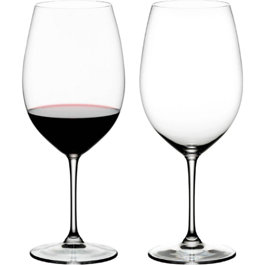 A set of two Riedel Vinum Red Wine glasses by Riedel—one filled with red wine and the other empty—are displayed side by side against a plain white background.